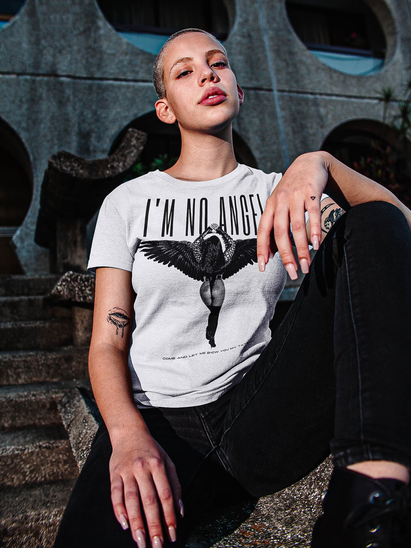 Fashion-forward girl with a buzz cut, striking a confident pose in a 'I'm No Angel Cher' T-shirt by Gllamazon, showcasing alternative beauty.
