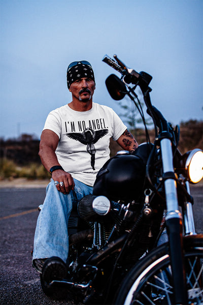 Serious biker man on his motorcycle, wearing 'I'm No Angel Cher' T-shirt by Gllamazon, portraying a strong, independent attitude.