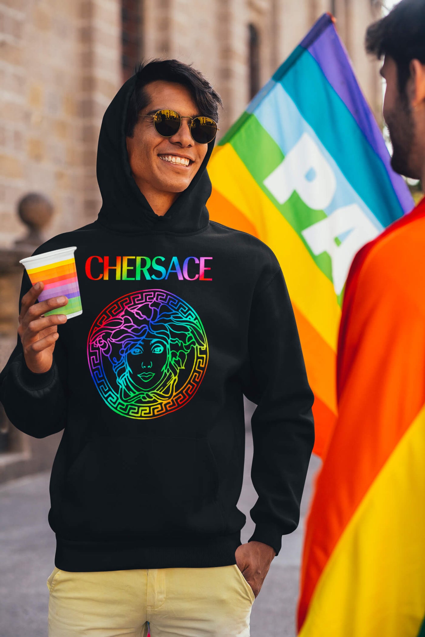 Man with a CHERSACE by Gllamazon hoodie and sunglasses at the Pride parade.